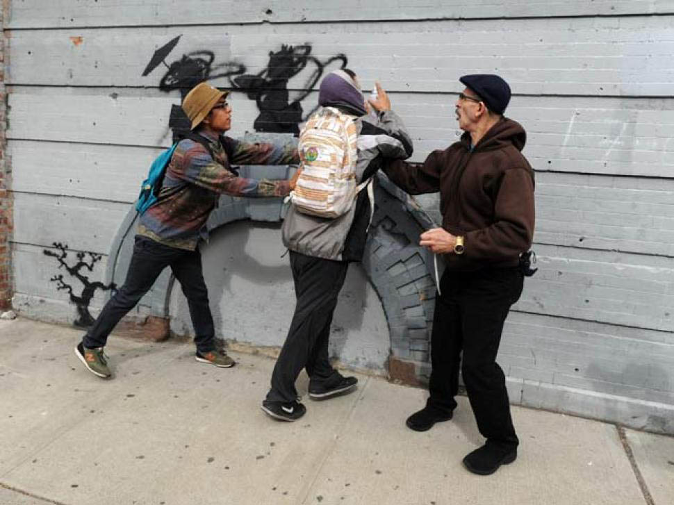The defacer of Banksy's work is quickly apprehended by bystanders.